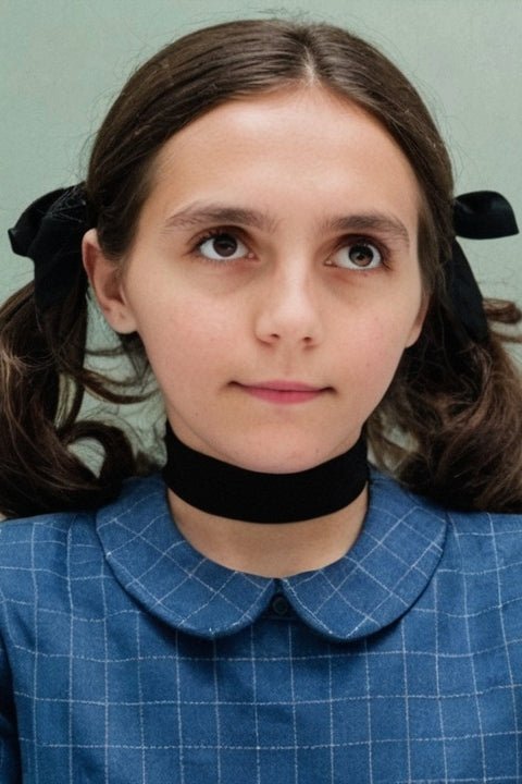 Une jeune fille portant une robe bleue et un collier, souriant joyeusement dans un environnement ensoleillé.